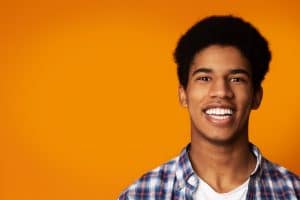 Teeth Whitening. Afro Guy Smiling Widely on Yellow Studio Background with Copy Space