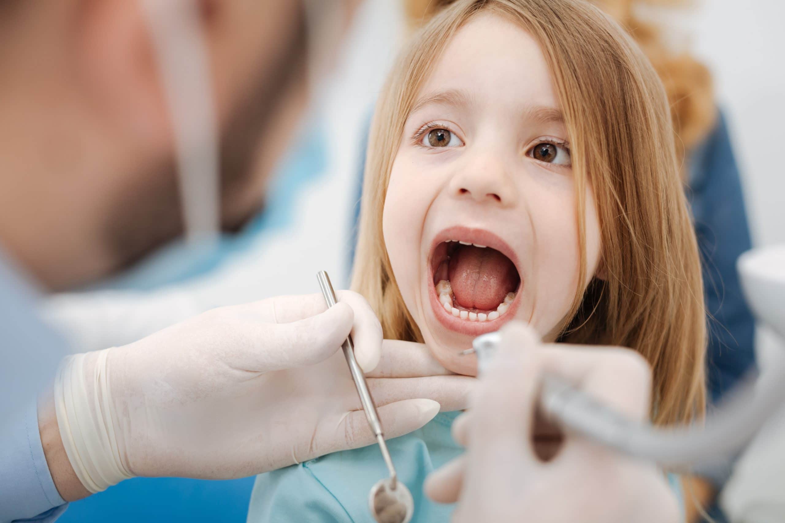 Girl child keeping her mouth open while dentist performs checkup.