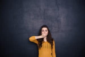 Young woman covering her mouth over black background