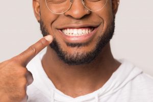 Close up of happy african American man isolated on grey studio background show point at white teeth, excited biracial male demonstrate wide healthy smile after good service dental treatment