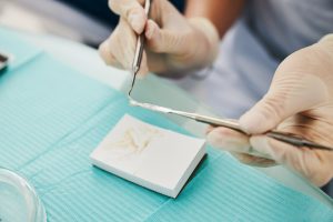 Orthodontist picking soft tooth filling from dental spatula with stomatological carver over foam plastic brick