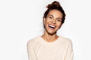 Portrait of cheerful model laughing at something. Pretty young woman in beige pullover. Brunette girl in good mood. Happiness and beauty concept. Isolated on white background