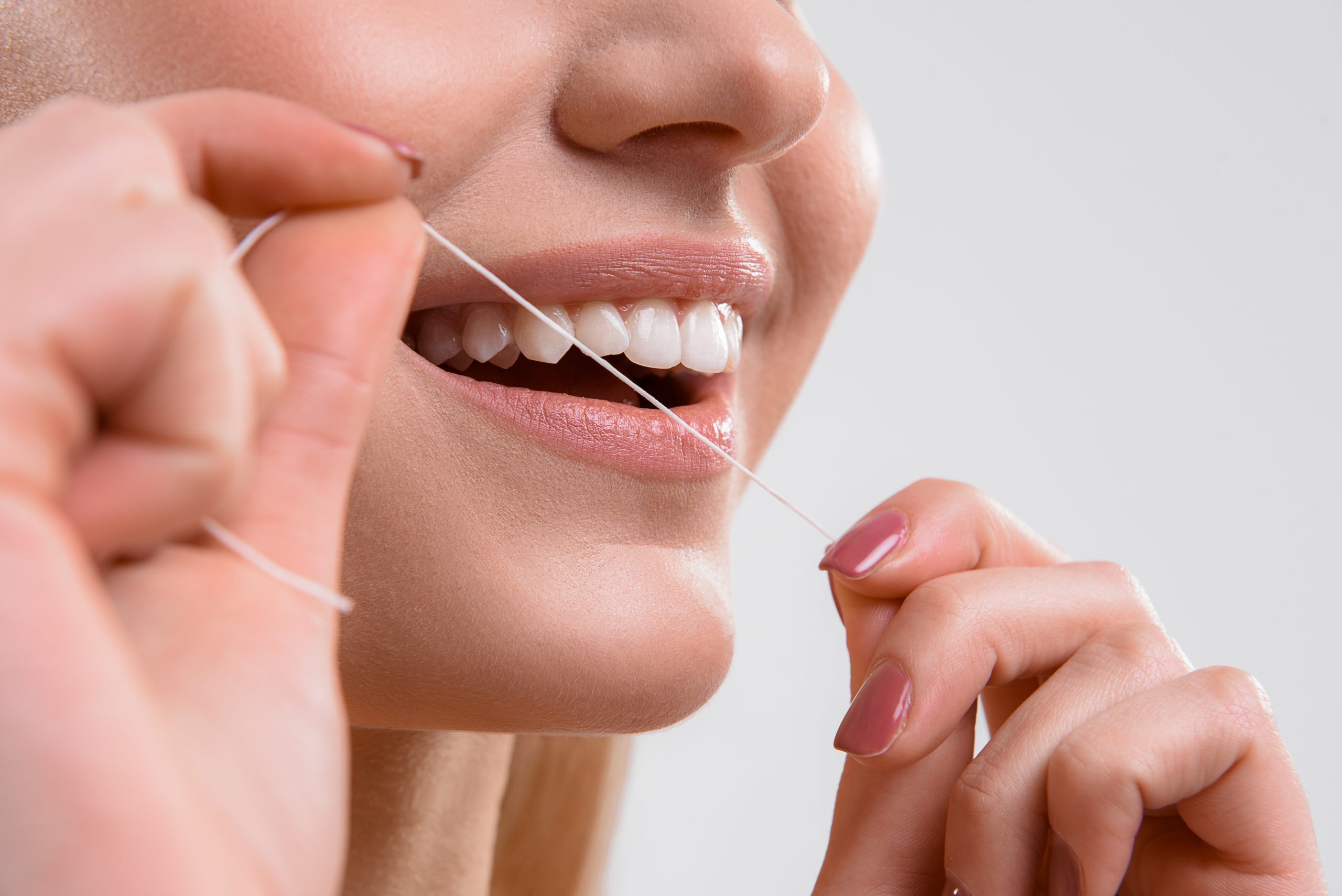 Close up of female mouth. Happy young woman is flossing her teeth and smiling. Isolated