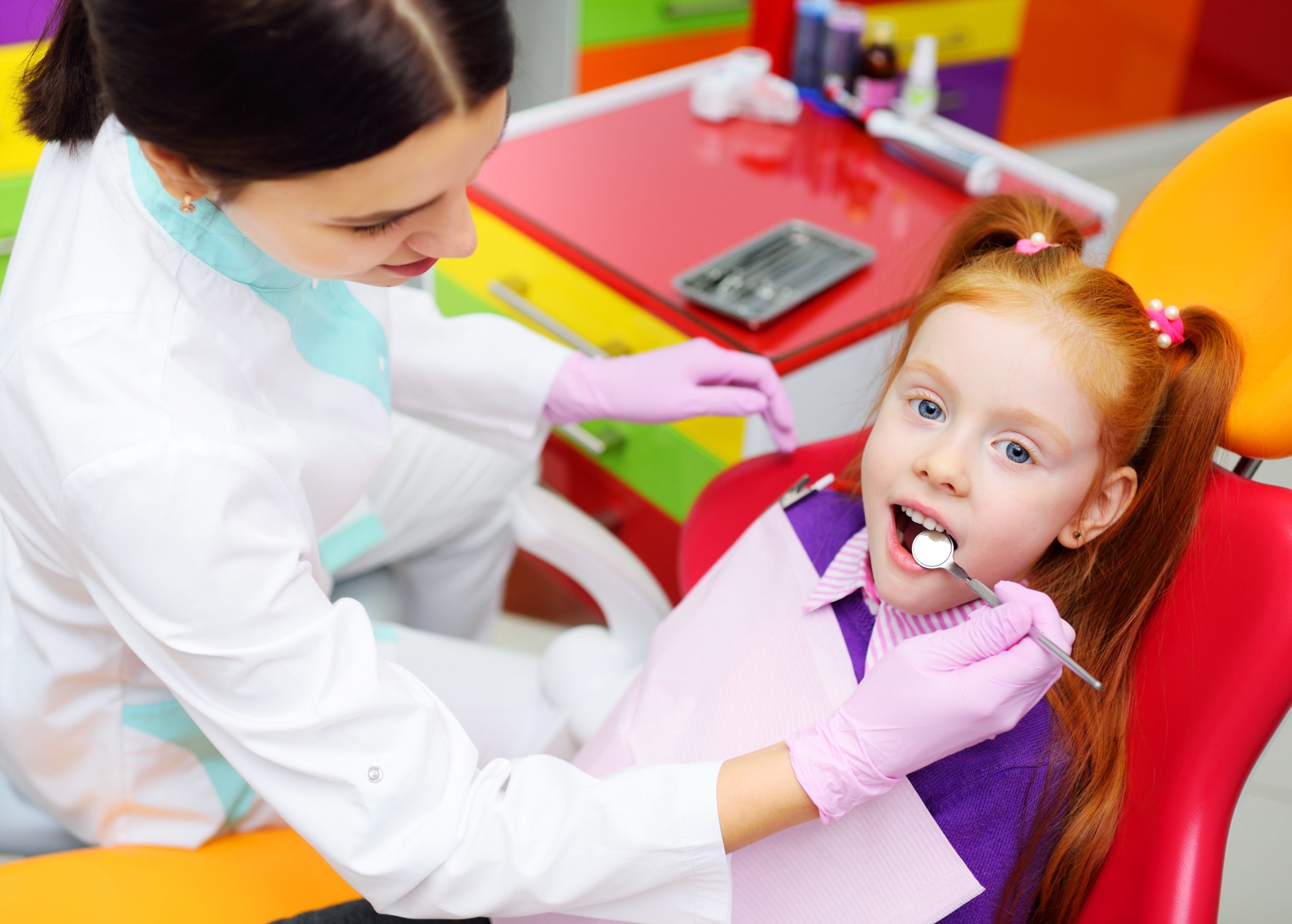 children's dentist examines the teeth and mouth of the child - a cute red-haired girl sitting in a dental chair. Pediatric dentistry