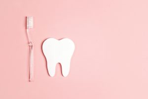 White paper tooth with toothbrush on pink background. Dental health concept. Dentist day concept. Flat lay, top view, copy space.