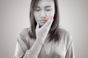 Suffering from toothache. Beautiful young woman suffering from toothache while standing against grey background