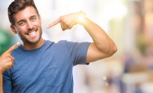 Young handsome man over isolated background smiling confident showing and pointing with fingers teeth and mouth. Health concept.