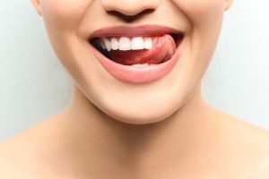 Young smiling woman licking her teeth on light background, closeup