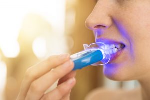 Woman is whitening teeth with special toothpaste and LED light at home. Beauty concept