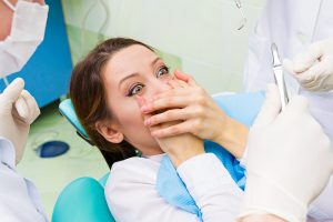 Closeup portrait young terrified girl woman scared at dentist visit, siting in chair, funny looking with fear, doesn't want dental procedure drilling tooth extraction isolated clinic office background