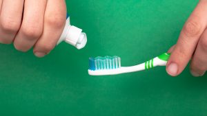 hand squeezes a toothpaste onto a toothbrush on a green background close-up. dental and oral care tooth decay.