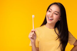 Happy woman take care tooth and holding toothbrush Young lady brushing her teeth Beautiful asian girl has beautiful tooth, white teeth   nice tooth alignment Yellow background, copy space Dental care