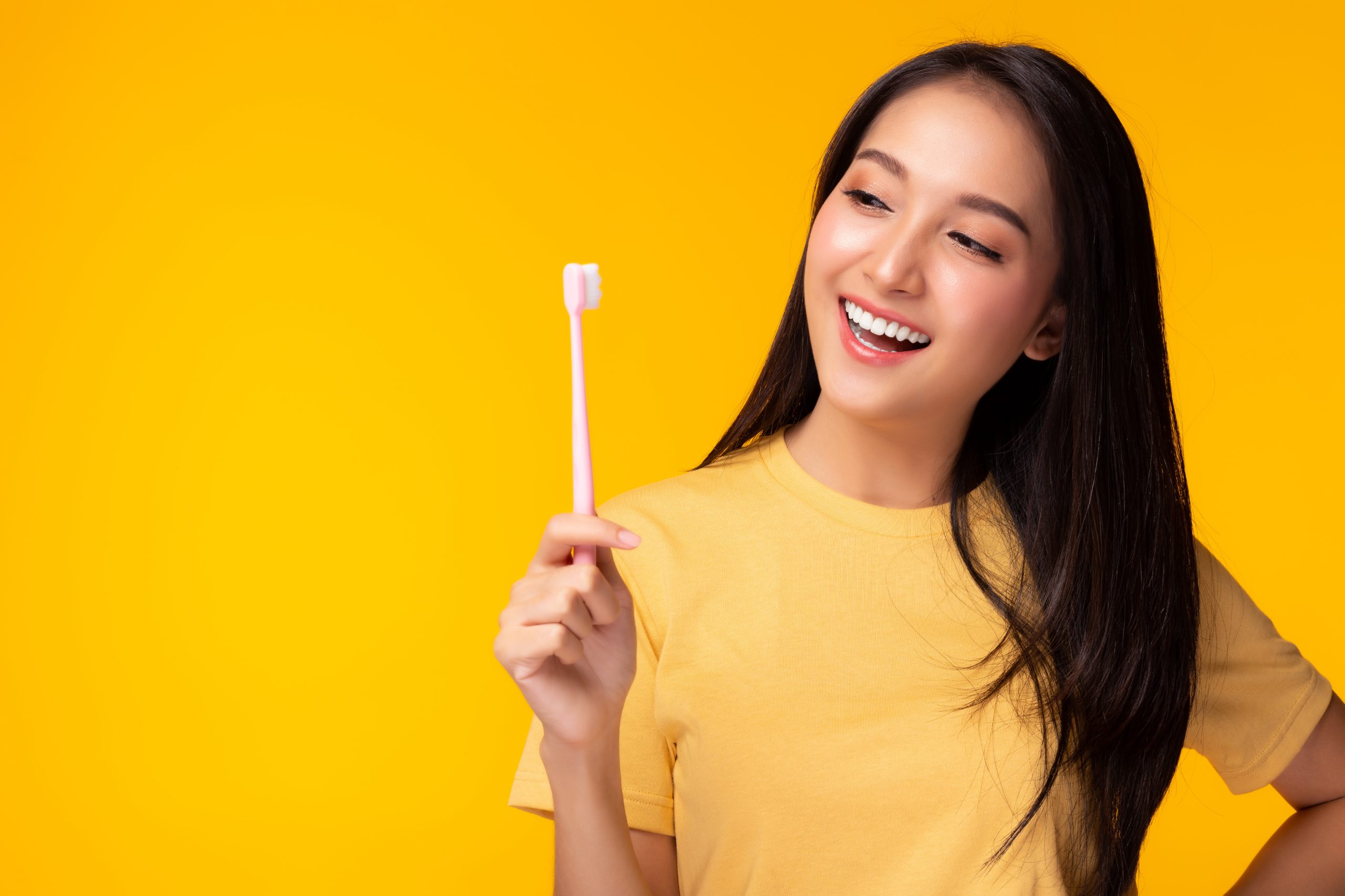 Happy woman take care tooth and holding toothbrush Young lady brushing her teeth Beautiful asian girl has beautiful tooth, white teeth nice tooth alignment Yellow background, copy space Dental care
