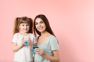 Little girl and her mother with mouthwash on color background, space for text. Teeth and oral care