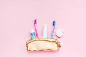 Teeth hygiene and oral dental care products in golden travel cosmetic purse kit pastel pink color background with copy space. Blank tube of toothpaste and toothbrushes. Flat lay, top view composition