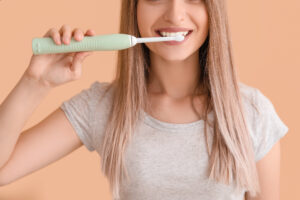 Young woman with electric tooth brush on color background