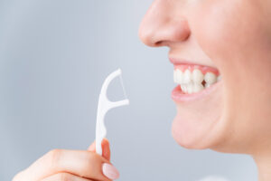 Close-up portrait of a beautiful caucasian woman with a flawless smile holding a toothpick with dental floss on a white background.