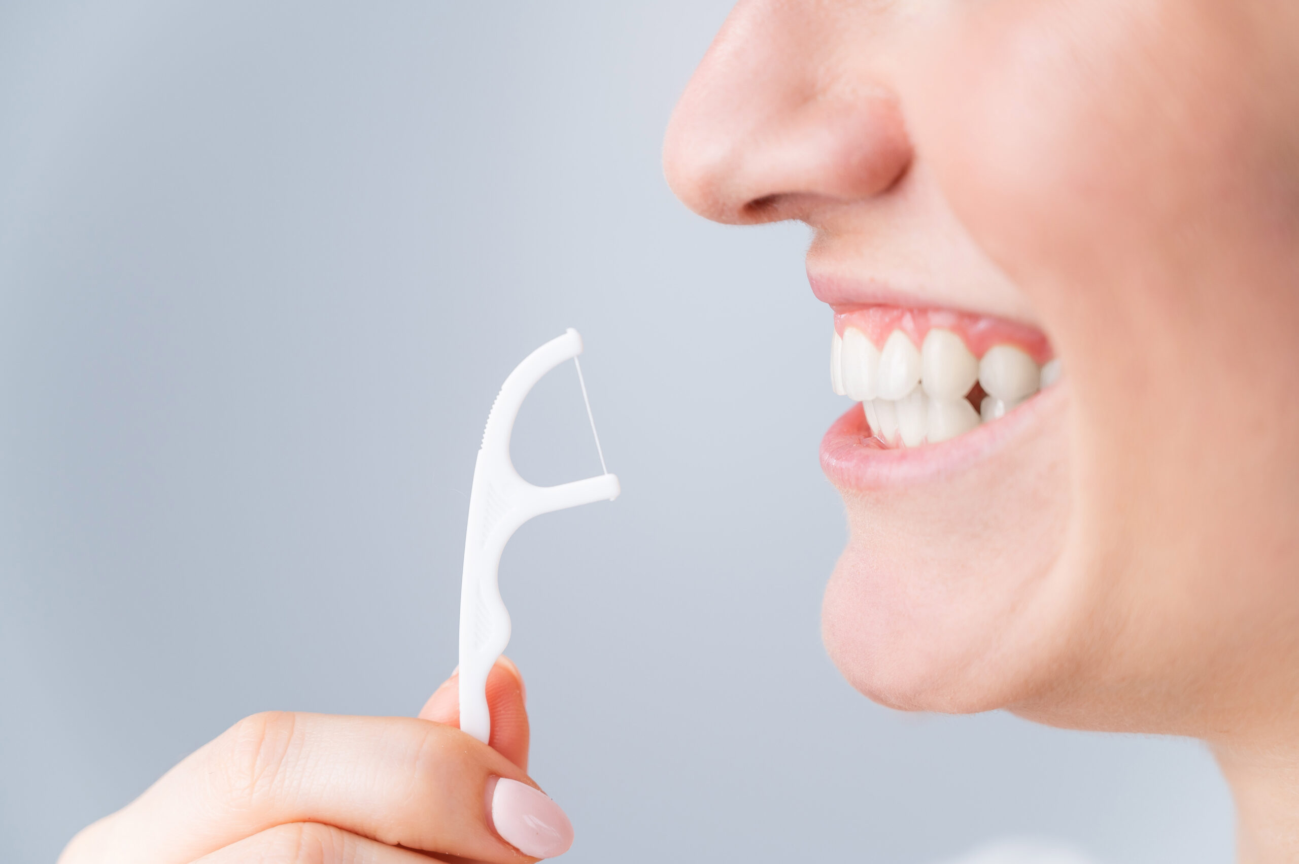 Close-up portrait of a beautiful caucasian woman with a flawless smile holding a toothpick with dental floss on a white background.