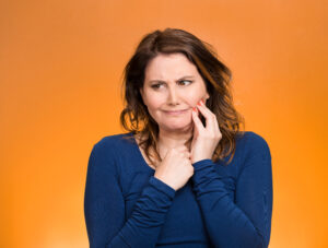 Portrait middle aged woman with sensitive tooth ache, crown problem crying from pain, touching outside mouth with hand isolated orange background. Negative emotion, facial expression feeling, health