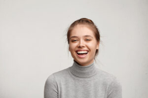 Headshot of good-looking lucky woman with tied hair pure skin and broad smile being happy to watch at camera. Sincere female with beautiful appearance wearing casual clothes isolated over white wall
