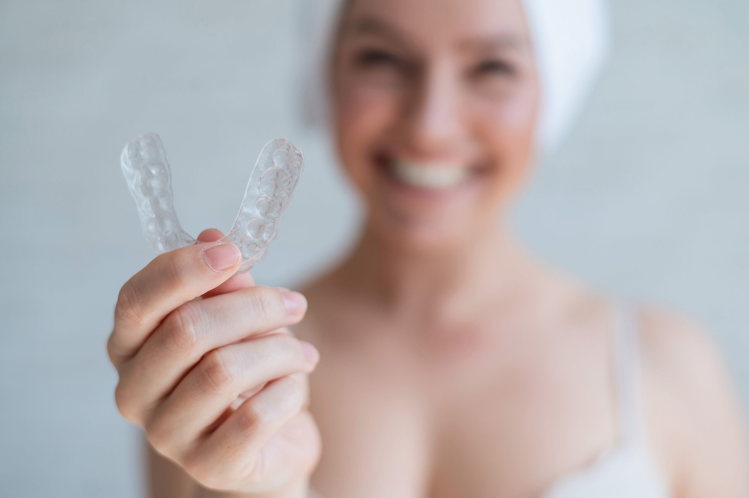 A woman with a towel on her head holds a whitening mouth guard for teeth. The girl aligns her teeth with the help of transparent night removable retainers. Orthodontic device for a perfect smile