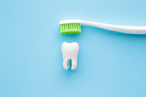 White tooth and toothbrush with green bristles on pastel blue ba