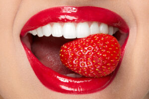 Lips. Woman With Red Lipstick And Strawberry. Close Up Of Plump Full Sexy Lips With Professional Lip Makeup Holding Berry In White Healthy Teeth. Beauty And Cosmetics Concept. High Resolution