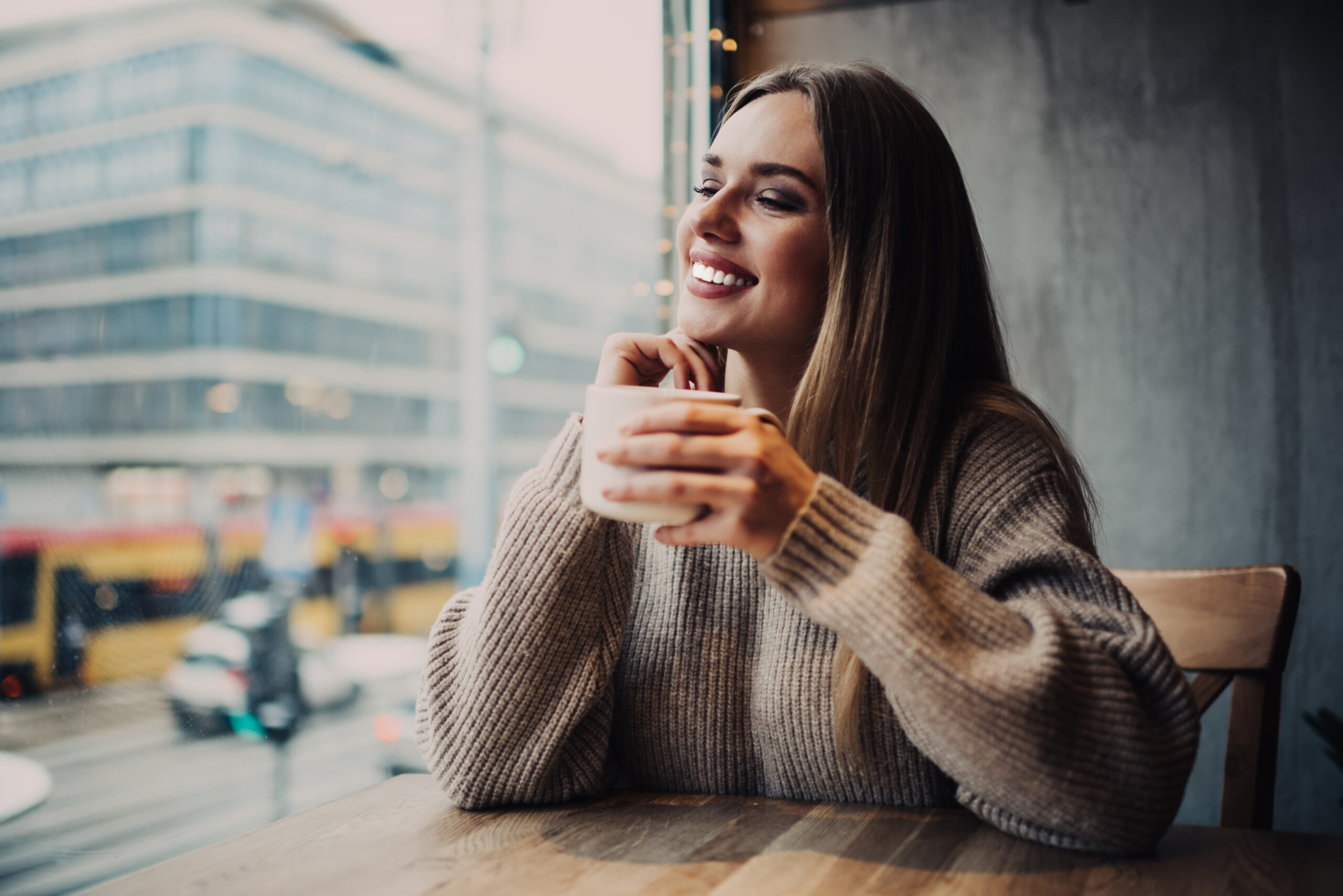 Cheerful hipster girl 20s with perfect veneers laughing during resting time in cafe interior, sincerely female customer with tea cup for warming smiling during cafeteria recreation on weekend