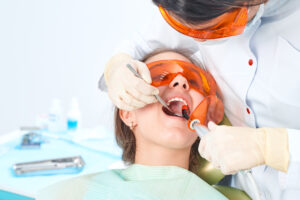 Girl child at the doctor. Dentist places a filling on a tooth with dental polymerization lamp in oral cavity. over clinic background.