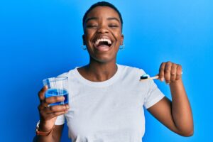 Young african american woman holding glass of mouthwash and toothbrush for fresh breath smiling and laughing hard out loud because funny crazy joke.