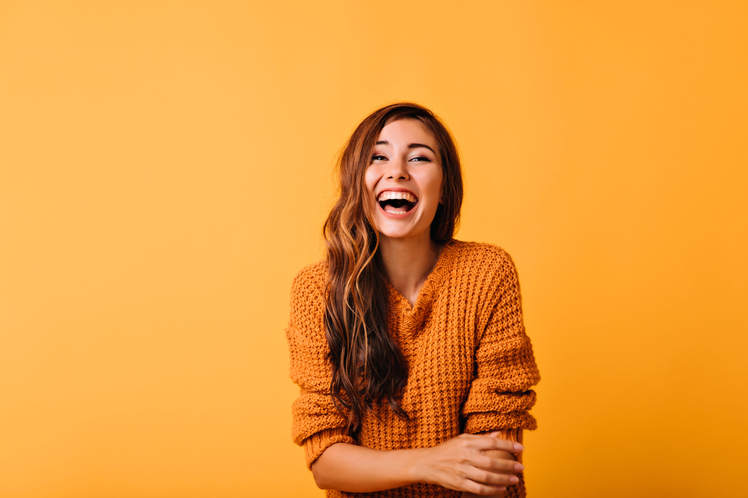 Enthusiastic white girl with long shiny hair laughing on orange background. Excited european woman posing with sincere smile.