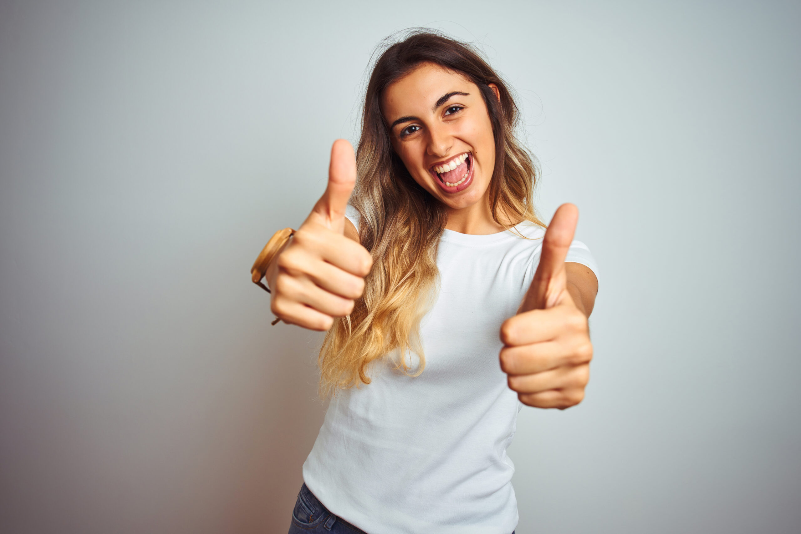 Young beautiful woman wearing casual white t-shirt over isolated background approving doing positive gesture with hand, thumbs up smiling and happy for success. Winner gesture.