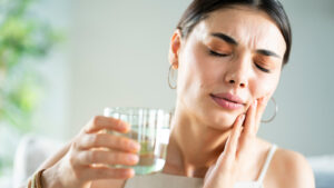 Young woman with sensitive teeth and hand holding glass of water