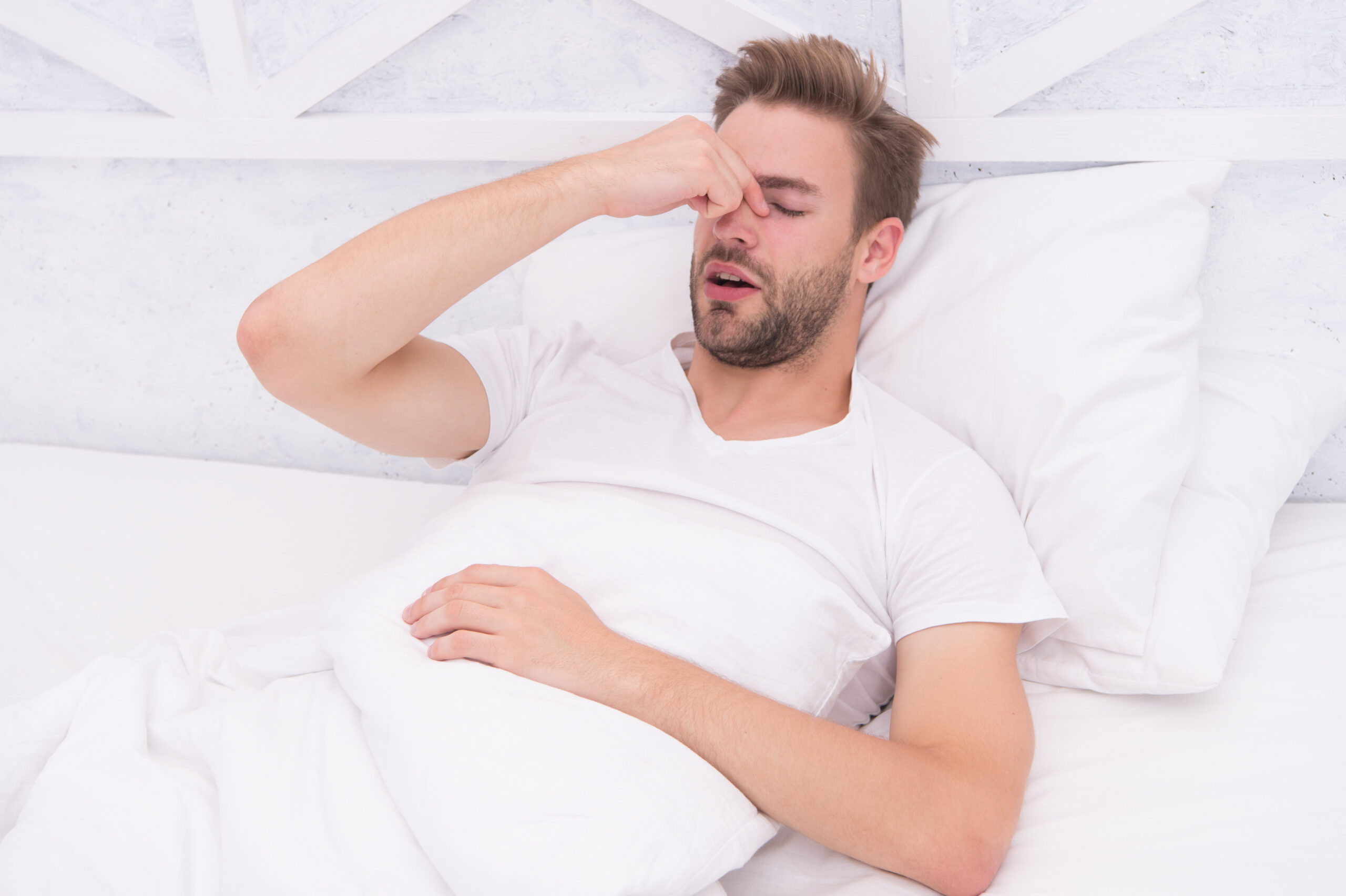 Snoring can increase risk headaches. Common symptom of sleep apnea. Causes of early morning headache. Migraine headaches. Sleep problems can lead to headaches in morning. Handsome man relaxing in bed.