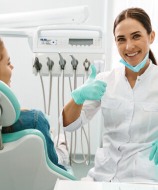 European mid dentist woman showing thumb up while working with patient in dental clinic